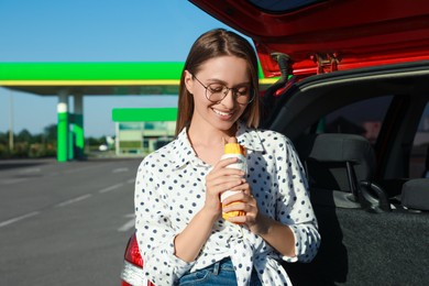 Beautiful young woman with hot dog near car at gas station