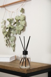 Reed diffuser and book on wooden table near white wall