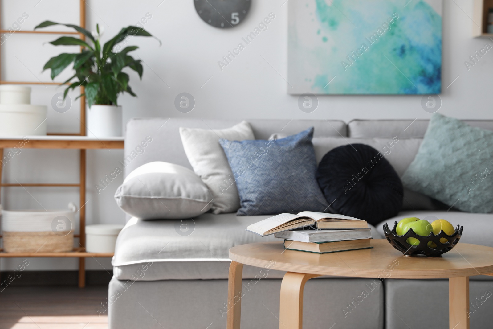 Photo of Table with books and apples near sofa in living room. Interior design