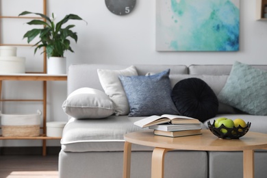 Table with books and apples near sofa in living room. Interior design