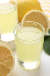 Photo of Shot glasses with tasty limoncello liqueur and lemons on table, closeup