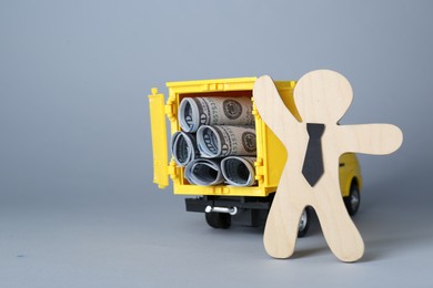 Economic profit. Wooden figure and toy truck with banknotes on light grey background, space for text