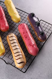 Cooling rack with different tasty glazed eclairs on grey table, above view