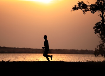 Photo of Young man running near river at sunset