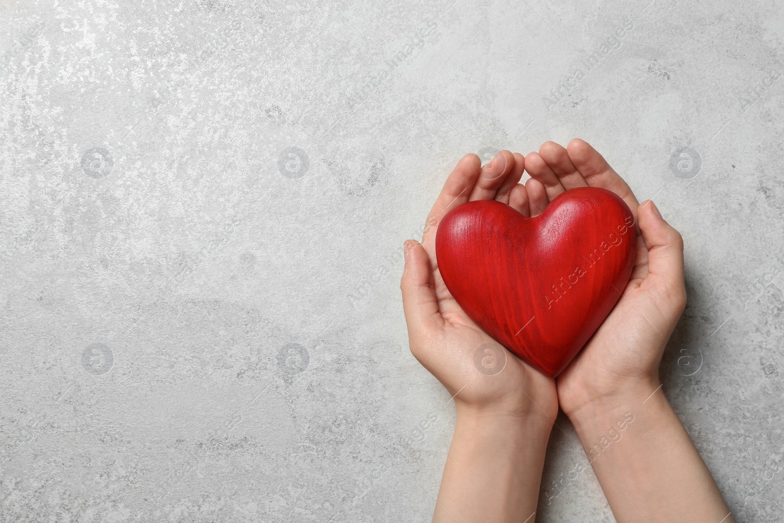 Photo of Woman holding heart on grey stone background, top view with space for text. Donation concept