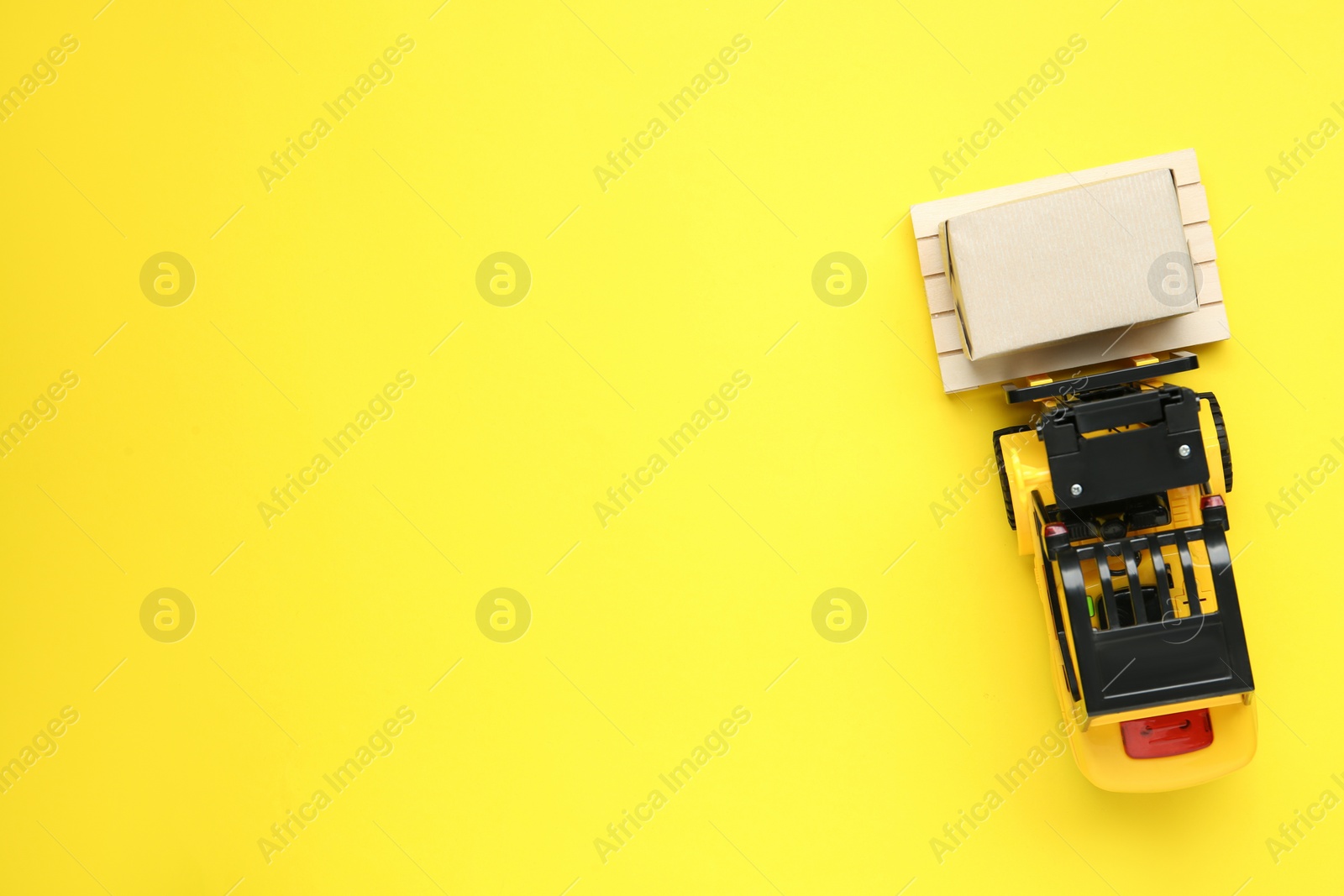 Photo of Toy forklift with wooden pallet and box on yellow background, top view. Space or text