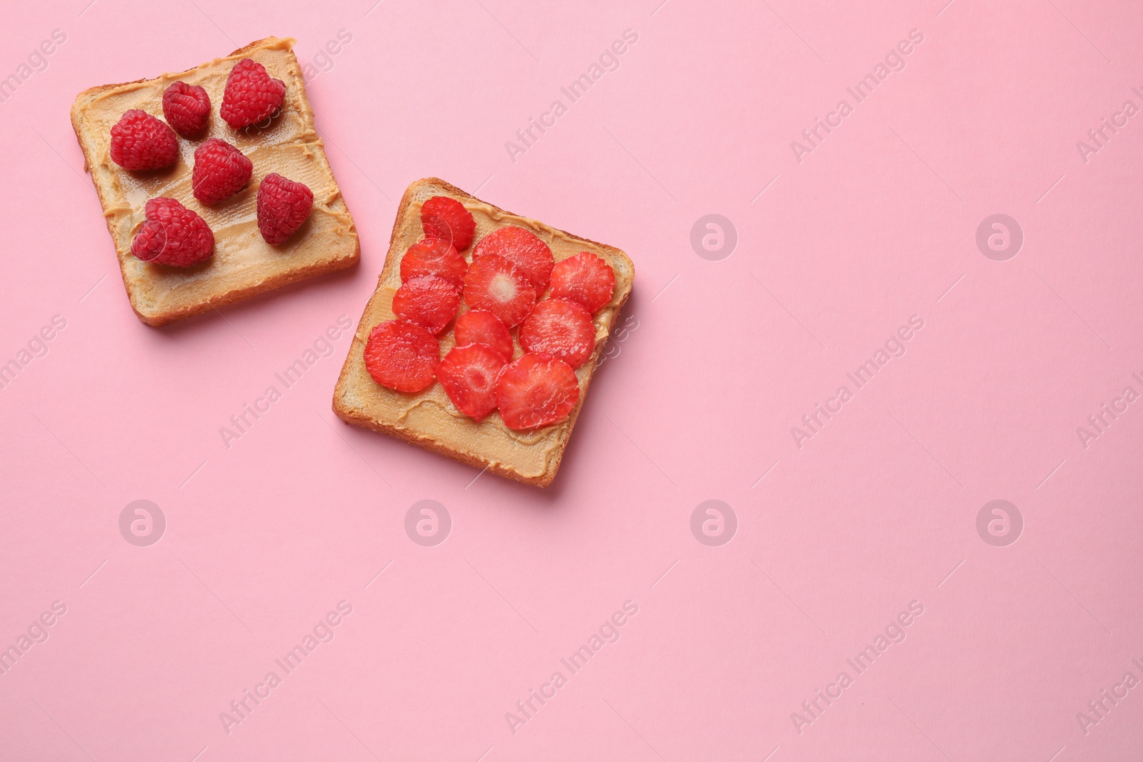 Photo of Tasty peanut butter sandwiches with fresh berries on pink background, flat lay. Space for text