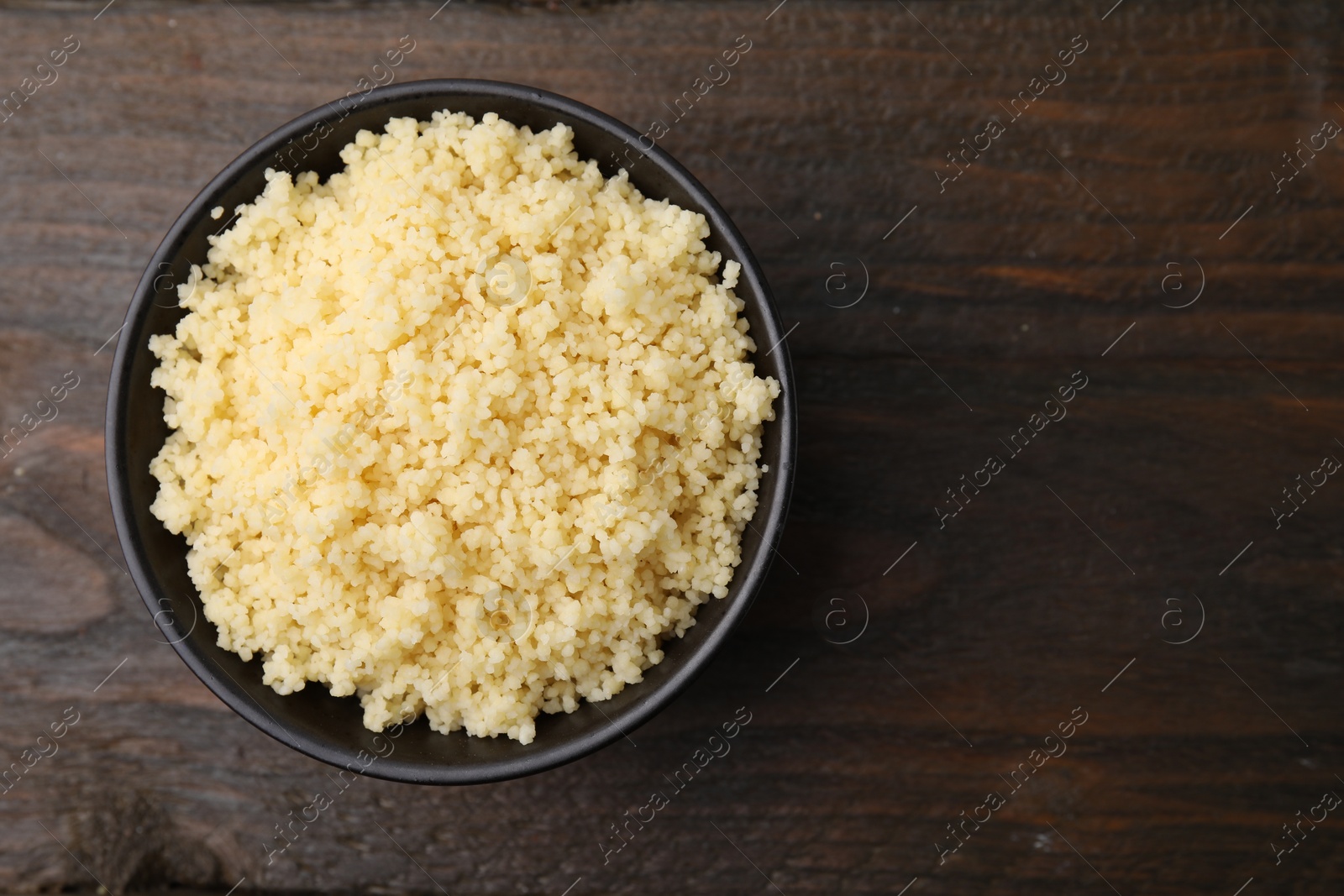 Photo of Tasty couscous in bowl on wooden table, top view. Space for text