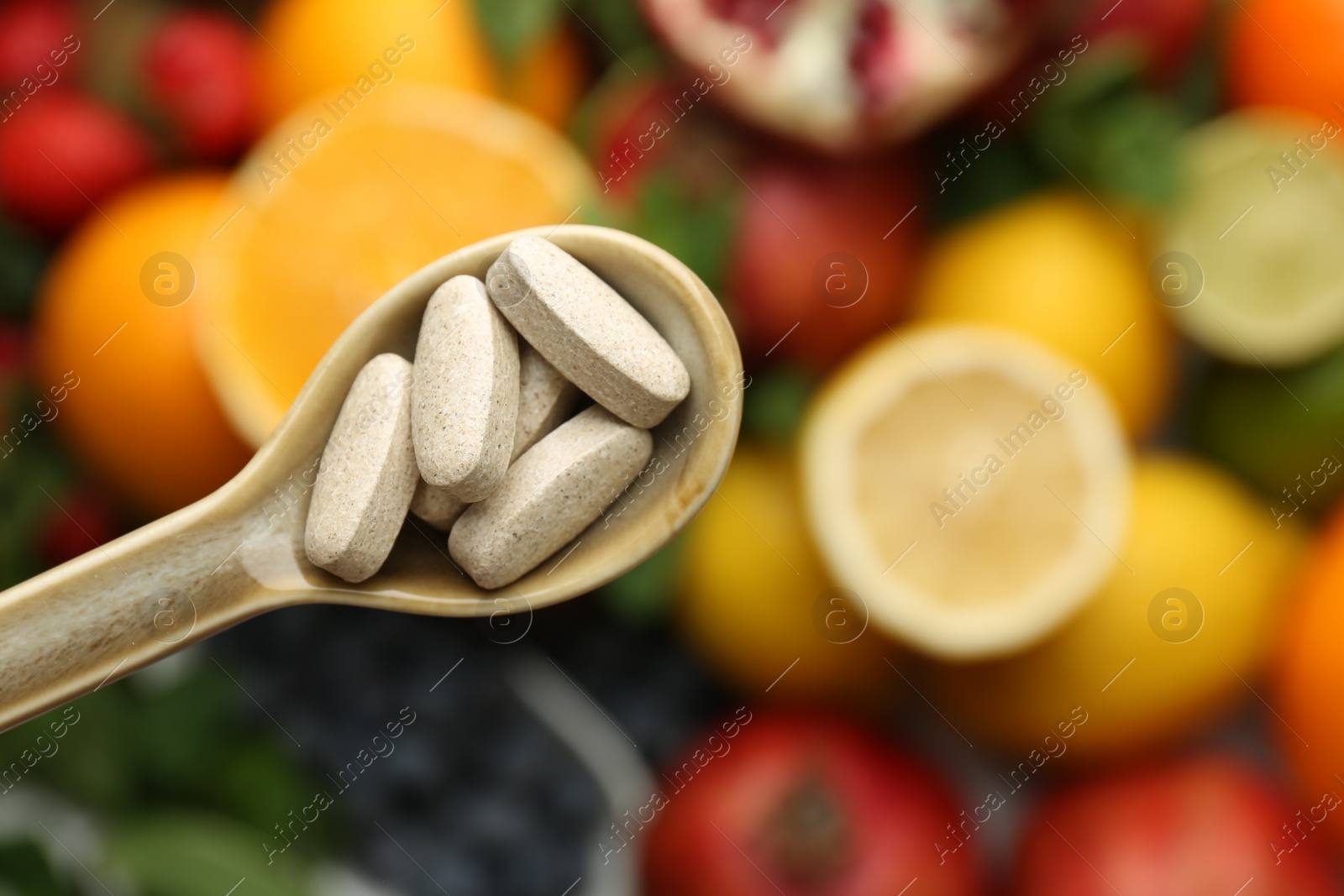 Photo of Vitamin pills in spoon over fresh fruits, top view. Space for text