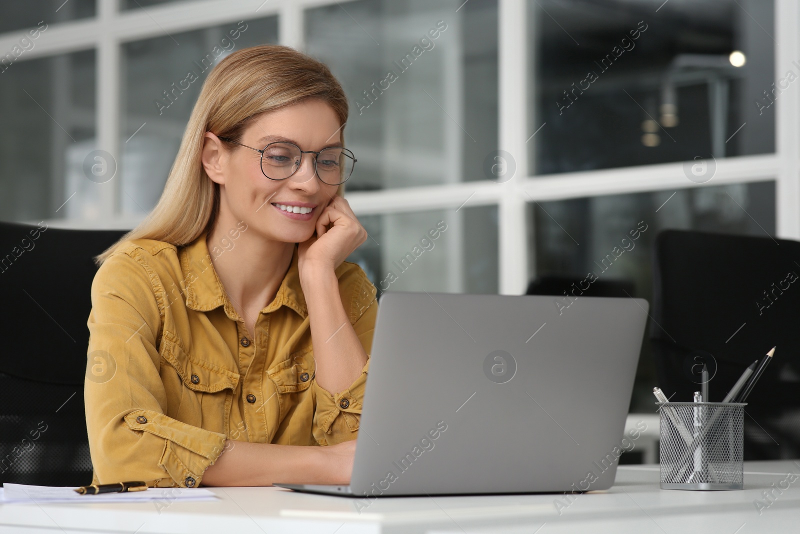 Photo of Woman working on laptop at white desk in office