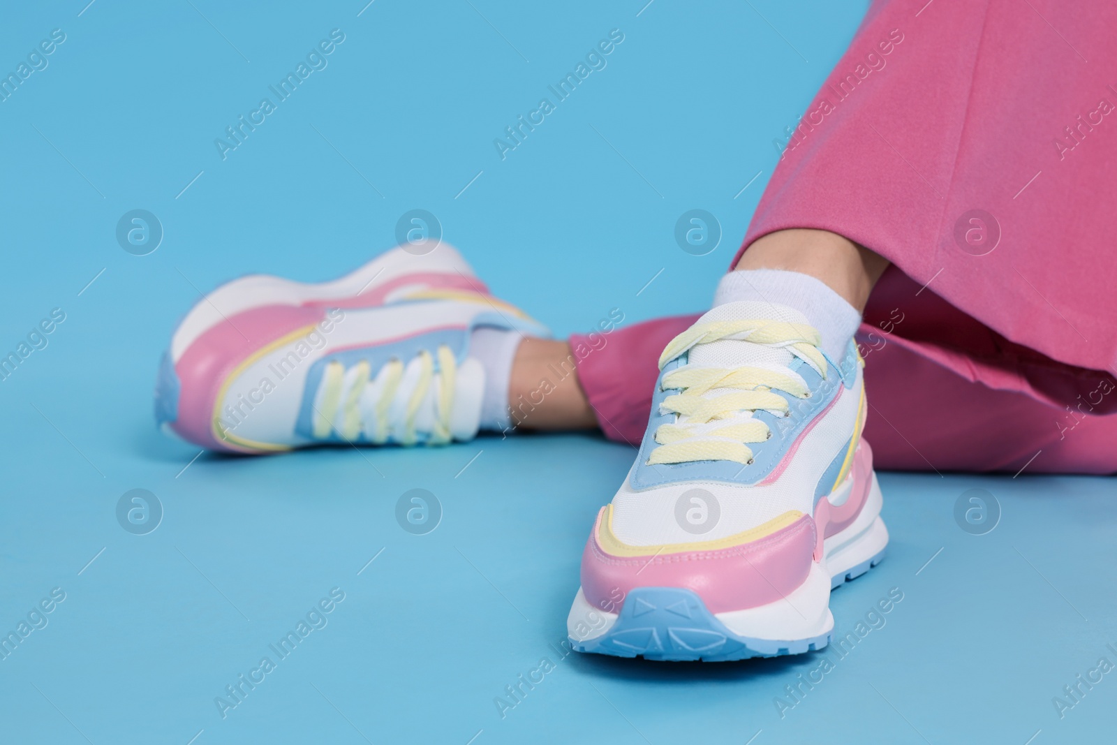 Photo of Woman wearing pair of new stylish sneakers on light blue background, closeup