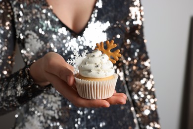 Photo of Woman holding tasty Christmas cupcake with cream and snowflake cookies on light background, closeup