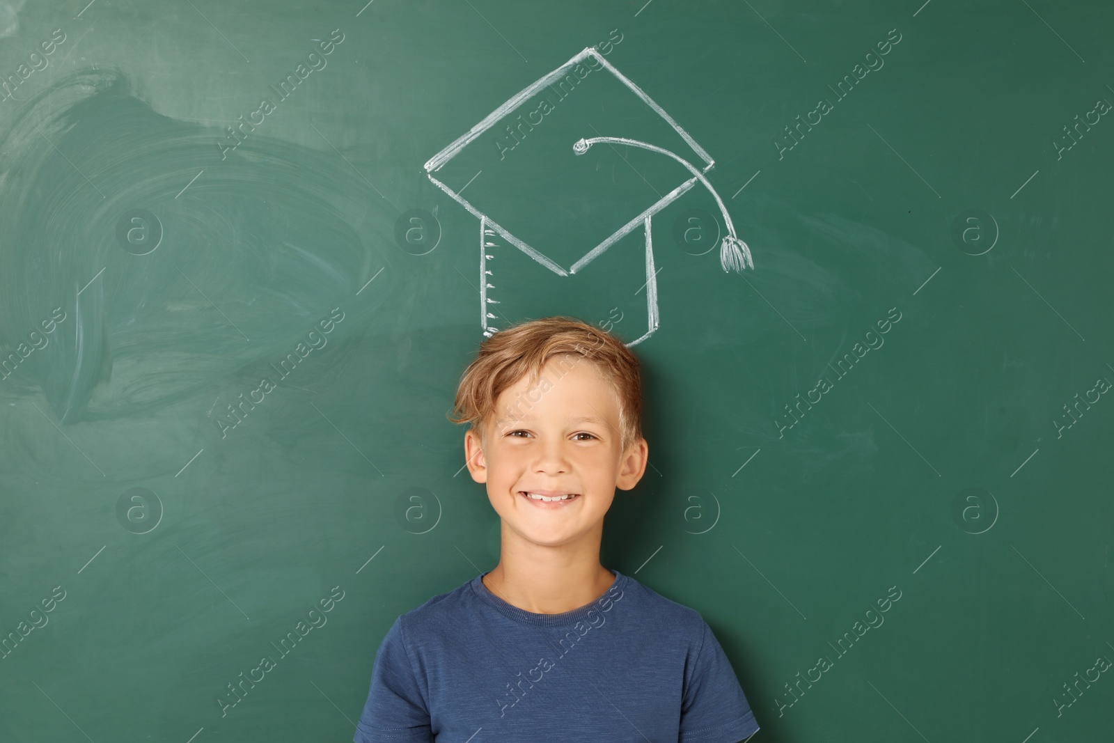 Photo of Little school child near chalkboard with drawing of graduate cap