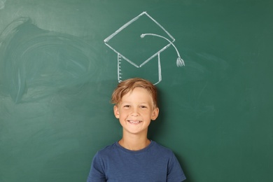 Little school child near chalkboard with drawing of graduate cap