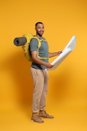 Photo of Happy tourist with backpack and map on yellow background