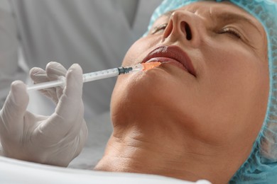 Photo of Doctor giving lips injection to senior woman in clinic, closeup. Cosmetic surgery