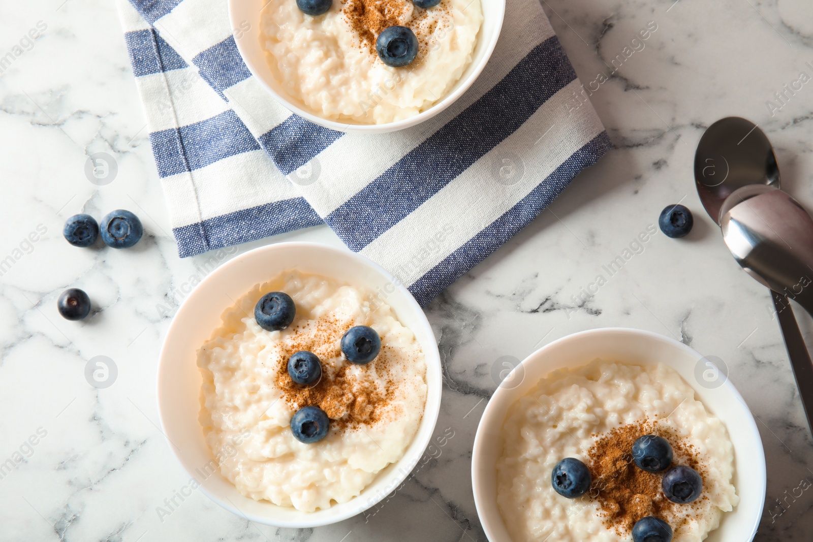 Photo of Creamy rice pudding with cinnamon and blueberries in bowls served on marble table, top view