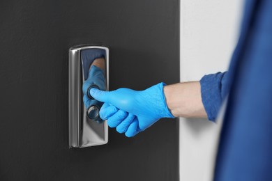 Photo of Man in glove pressing elevator call button, closeup. Protective measure