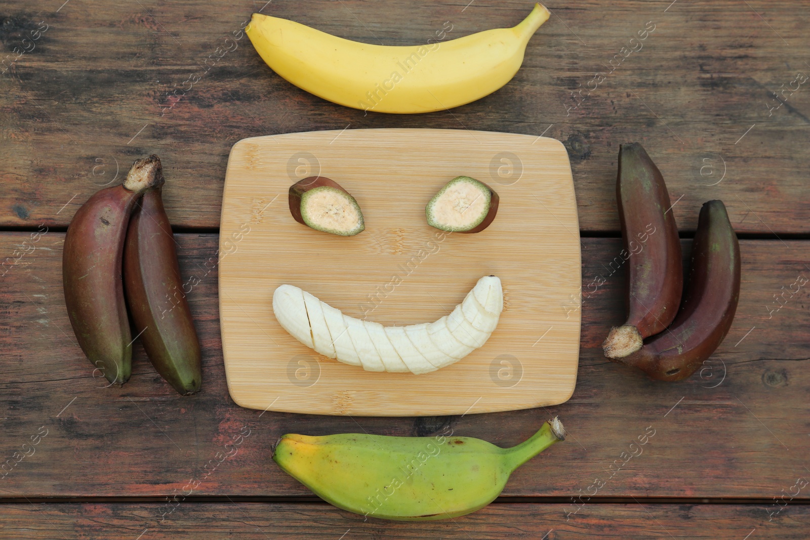 Photo of Smiley face made with banana slices and fruits on wooden table, flat lay