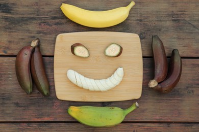 Photo of Smiley face made with banana slices and fruits on wooden table, flat lay