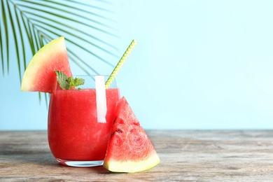 Photo of Tasty summer watermelon drink in glass and sliced fruit on table against color background. Space for text