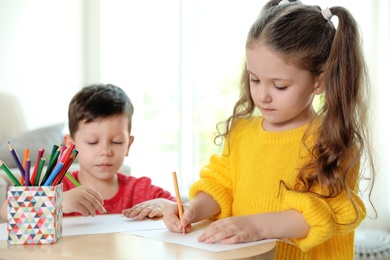 Photo of Cute little boy and girl drawing at table in living room