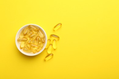 Photo of Vitamin capsules in bowl on yellow background, flat lay. Space for text