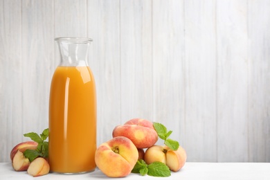 Photo of Natural peach juice and fresh fruits on white wooden table. Space for text