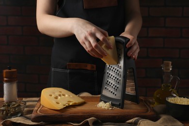 Photo of Woman grating cheese at wooden table, closeup