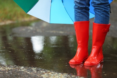 Photo of Woman with umbrella and rubber boots in puddle, closeup. Rainy weather