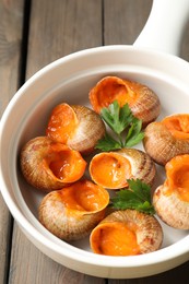 Delicious cooked snails with parsley in bowl on table, closeup