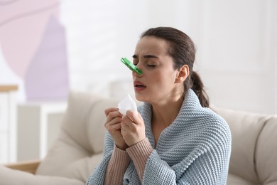 Photo of Young woman with clothespin suffering from runny nose in living room