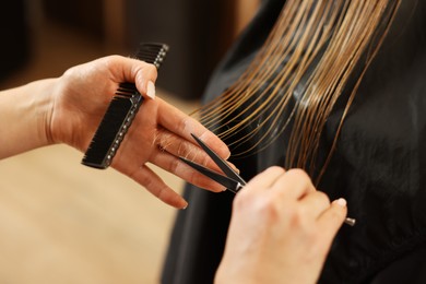 Photo of Professional hairdresser cutting girl's hair in beauty salon, closeup