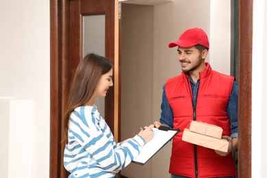 Photo of Woman receiving parcels from delivery service courier indoors