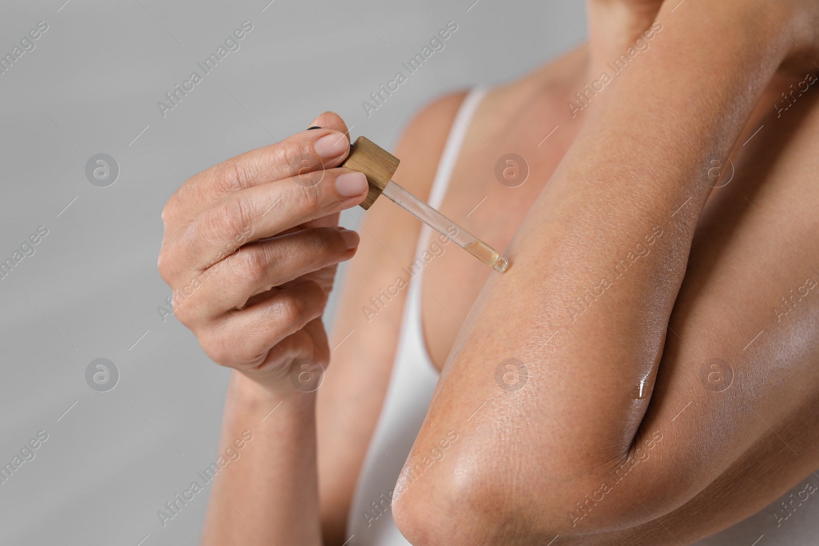 Photo of Woman applying body oil onto arm on grey background, closeup