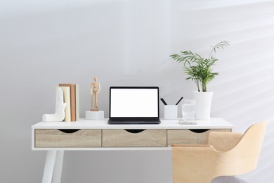 Photo of Stylish workplace with laptop, houseplant and stationery on wooden table near white wall