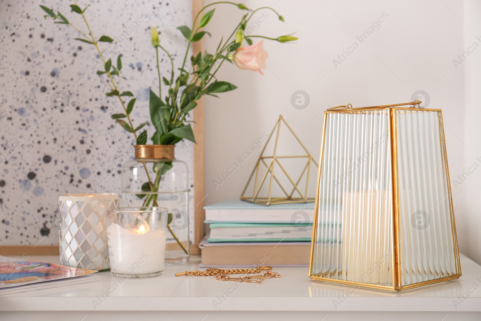 Photo of Stylish holder with burning candle, books and decor on white table