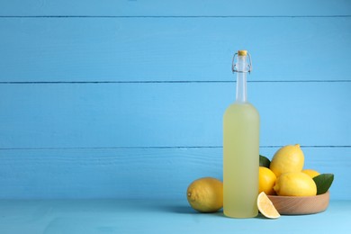 Photo of Bottle of tasty limoncello liqueur, lemons and green leaves on light blue table, space for text