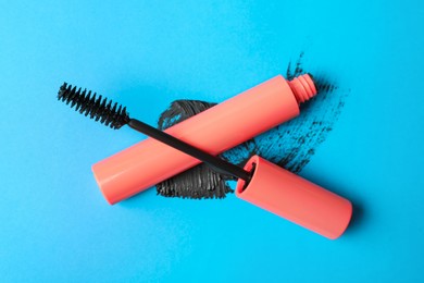 Photo of Mascara for eyelashes and smear on light blue background, flat lay. Makeup product