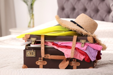 Photo of Vintage suitcase full of clothes on bed indoors