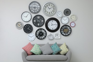 Sofa and many different clocks hanging on white wall in room