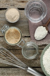Photo of Leaven, flour, whisk and water on wooden table, flat lay