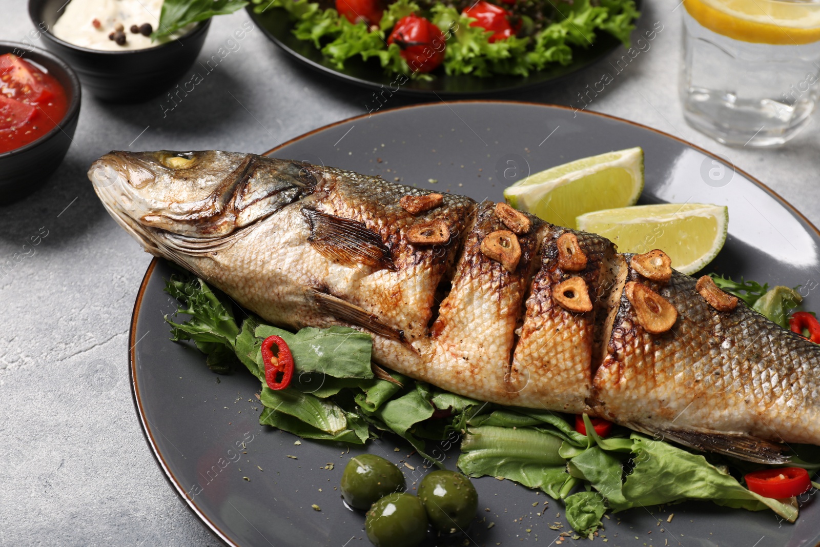 Photo of Delicious sea bass fish and ingredients on light grey table, closeup