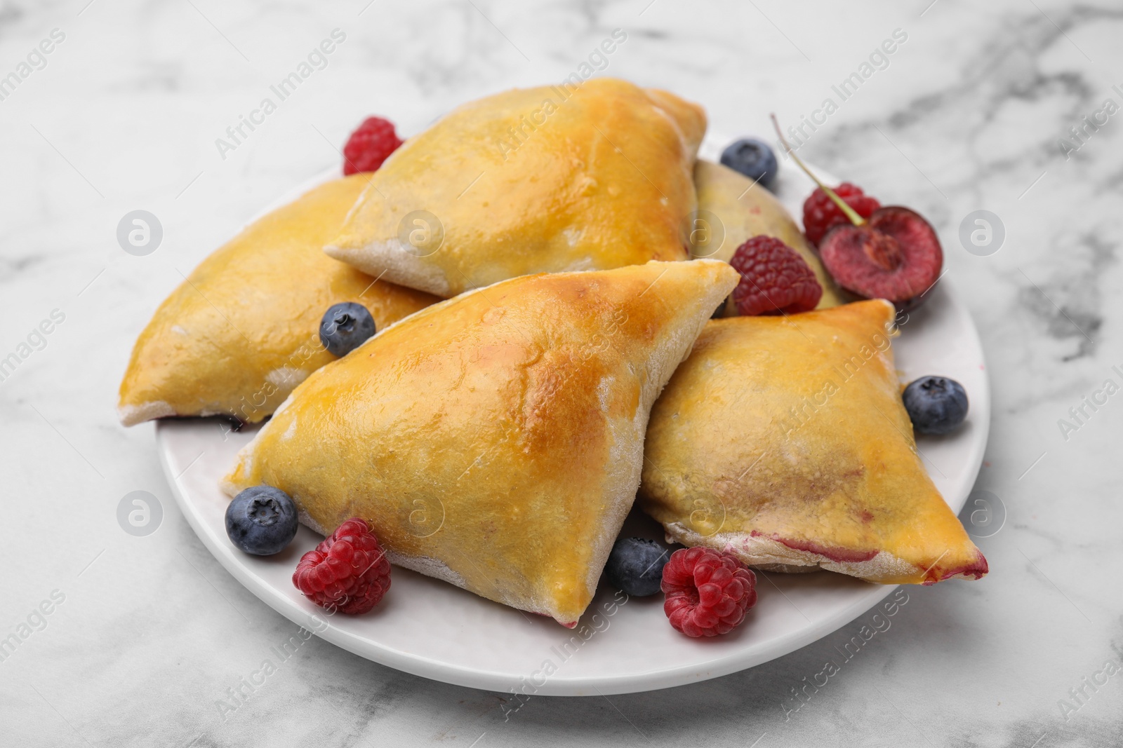 Photo of Delicious samosas with cherry and berries on white marble table, closeup