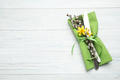 Top view of cutlery set with floral decor on white wooden table, space for text. Easter celebration