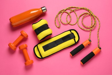 Photo of Yellow weighting agents and sport equipment on pink background, flat lay