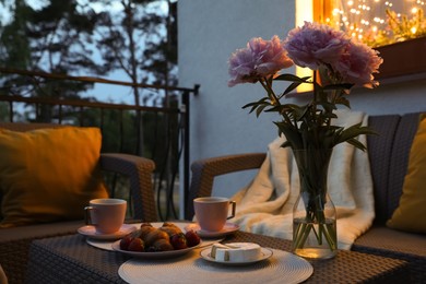 Photo of Rattan table with drink, food and flowers on outdoor terrace in evening