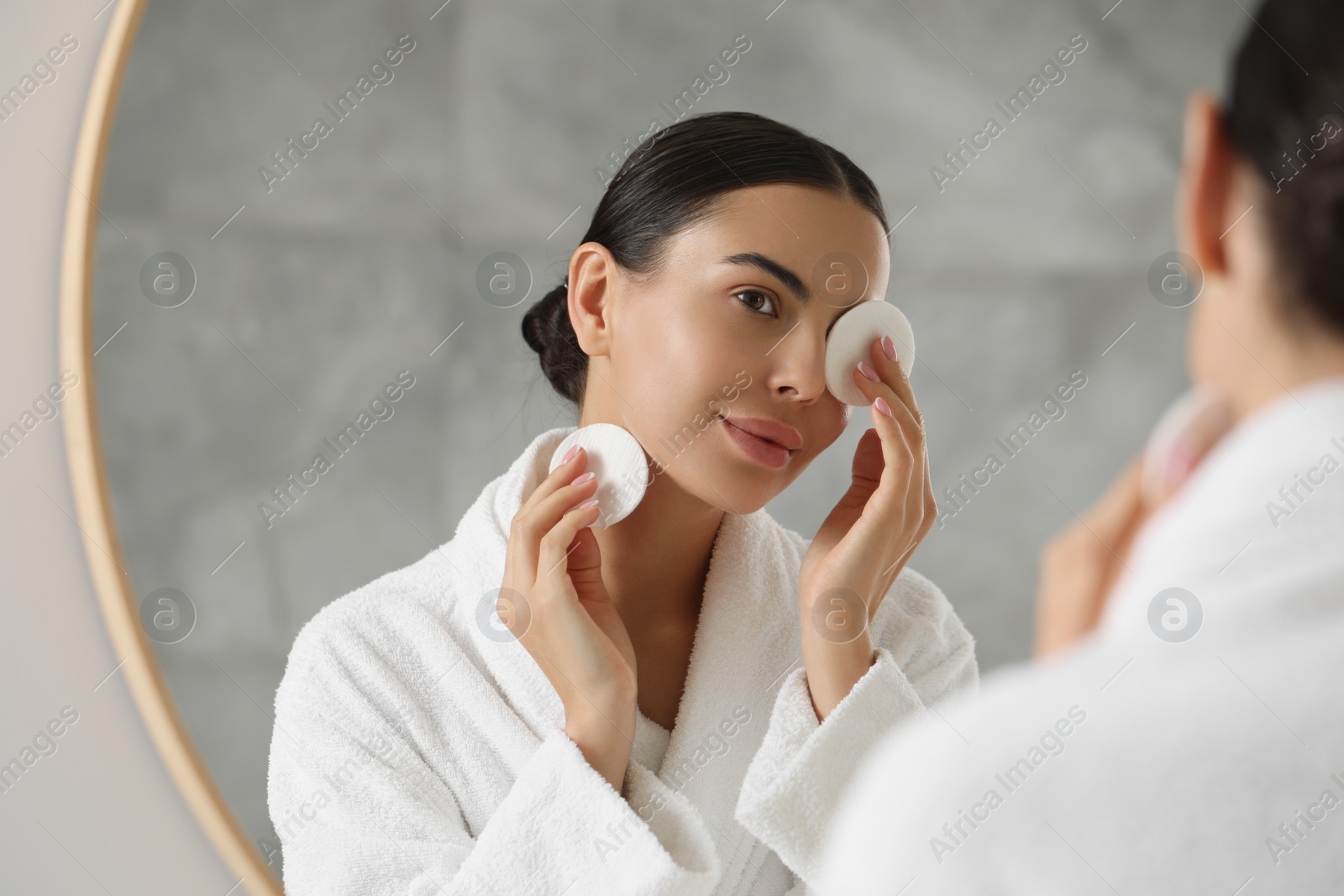 Photo of Beautiful woman removing makeup with cotton pads near mirror indoors