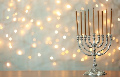 Photo of Hanukkah menorah with candles on table against blurred lights