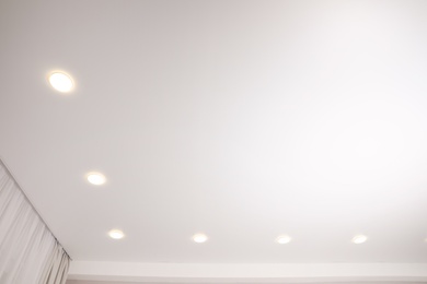 Photo of White stretch ceiling with spot lights in room, low angle view